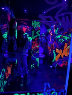 people are standing in the dark with neon lights and graffiti on the walls behind them