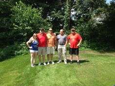 a group of people standing next to each other on a lush green field with trees in the background