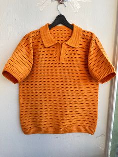 an orange knitted sweater hanging on a white wall next to a black hanger