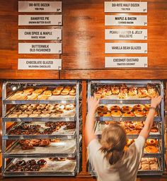 a woman reaching for donuts in a display case at a doughnut shop with signs on the wall