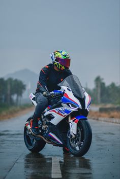 a man riding on the back of a motorcycle down a wet road