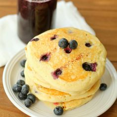 stack of pancakes with blueberries and syrup on plate next to glass of juice in background