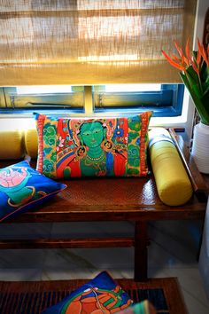 a wooden bench topped with pillows next to a vase filled with orange and green flowers