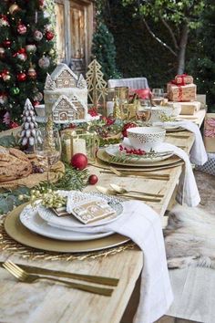 an outdoor table set for christmas with gold and white plates, silverware and candles