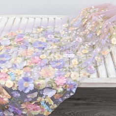 a blanket with flowers on it is sitting on a wooden bench next to a white fence