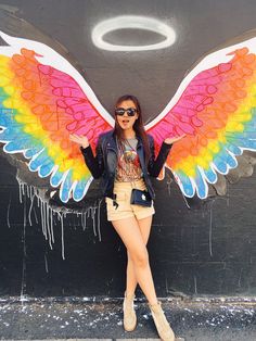 a woman wearing sunglasses and a jacket with wings painted on the side of a building