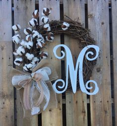 a cotton wreath with the letter m on it and a ribbon tied around it sitting on a wooden fence