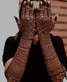 a woman holding her hands up to her face with henna tattoos on it's arms