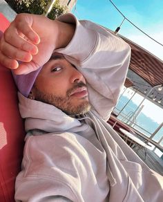 a man in a hoodie is sitting on a boat and pointing at the camera