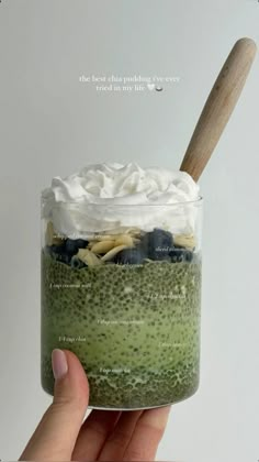 a hand holding up a jar filled with green smoothie and whipped cream on top