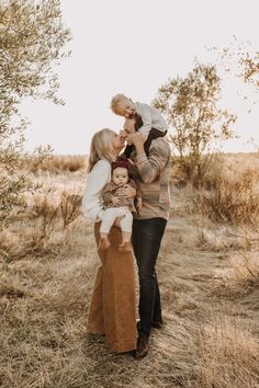 a man and woman kissing while holding their baby in the middle of an open field