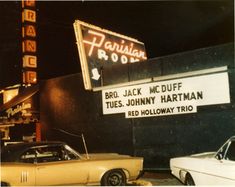 the marquee sign is lit up in front of two old cars parked outside