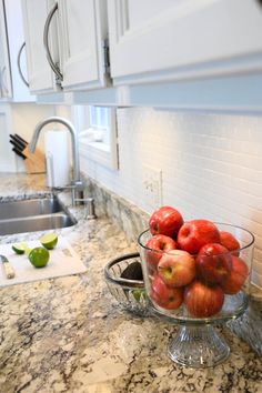 a glass bowl filled with apples on top of a kitchen counter