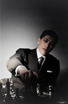 a man in a suit playing chess with his hand on the board and looking down