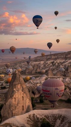 many hot air balloons are flying in the sky above some rocks and mountains at sunset