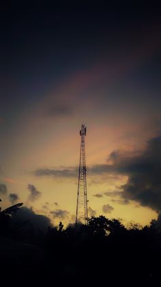 a tall tower sitting next to a forest under a sky filled with clouds at sunset