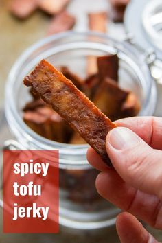 a hand holding a piece of bacon in a glass jar next to other food items