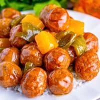 a white plate topped with meatballs covered in green peppers and orange sauce next to rice