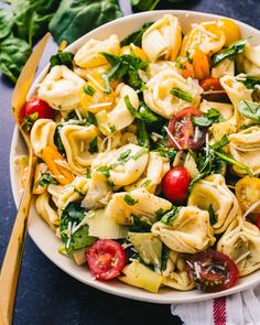 a white bowl filled with pasta salad next to a yellow fork and green leafy basil