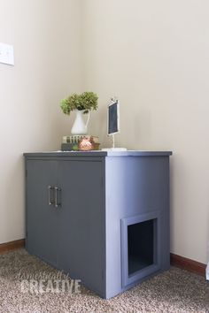 a gray cabinet with a white vase on top and a plant in the corner next to it