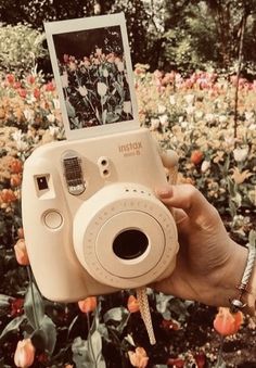 a person holding up a camera with flowers in the background