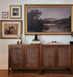 a painting hangs on the wall next to a sideboard with baskets and vases