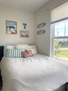 a white bed sitting in a bedroom next to a window with two surfboards hanging on the wall