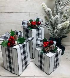 three present boxes decorated with holly, pine cones and berries are sitting on a white wooden surface