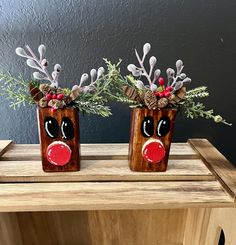 two wooden reindeer head vases with red nose and antlers on them, sitting on a table