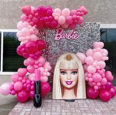 a barbie doll with pink balloons and lipstick on the table in front of a photo frame