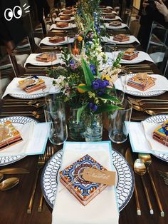 a long table with many plates and place settings on it, including desserts in glass vases