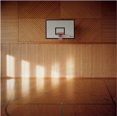 an empty basketball court with a basket in the middle and sunlight coming through the window