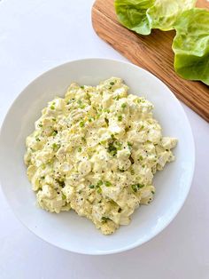 a white bowl filled with chicken salad next to lettuce on a cutting board