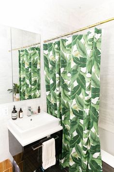 a bathroom with a sink, mirror and green leaf shower curtain in front of it