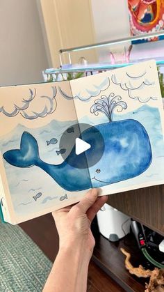 a person holding up an open book with a whale on it