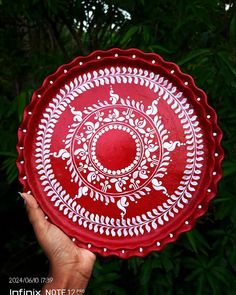 a hand holding a red plate with white designs on it