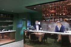 two men in tuxedos are sitting at a bar with bottles on the wall