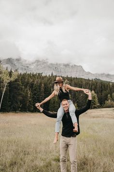 a man carrying a woman on his back in the middle of a field with mountains in the background