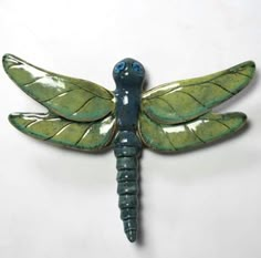 a blue and green dragon brooch sitting on top of a white wall