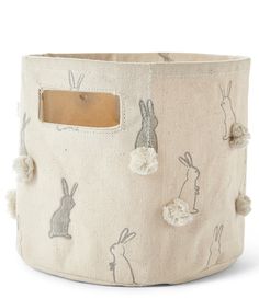 a white basket with rabbits and pom - poms on the inside, sitting in front of a white background