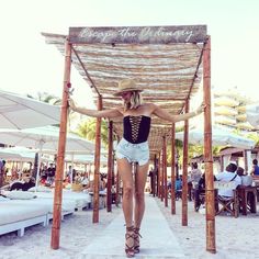 a woman walking down a beach covered in white umbrellas and straw chairs, with her arms stretched out