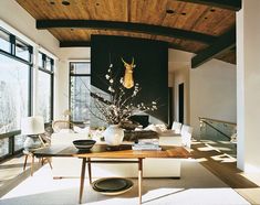 a living room filled with lots of furniture next to large windows and a wooden ceiling