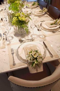 a table set with place settings and flowers in vases on the top, along with silverware