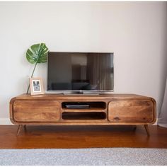 a wooden tv stand with a plant on top of it in front of a white wall