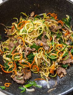 a wok filled with noodles and vegetables on top of a stove