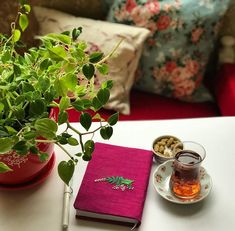 a table topped with a cup of tea next to a potted plant and a book