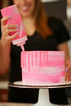 a woman is decorating a pink cake with icing on the top and holding a sprayer in her hand