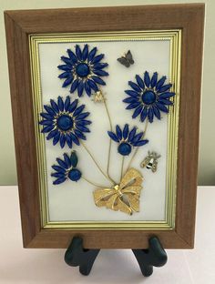 a blue and gold framed artwork with flowers in the center on a white table top