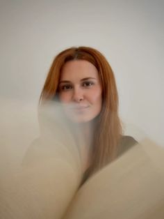 a woman with long red hair is looking at the camera while she's holding an open book