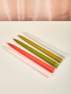 four different colored candles sitting next to each other on a white tableclothed surface